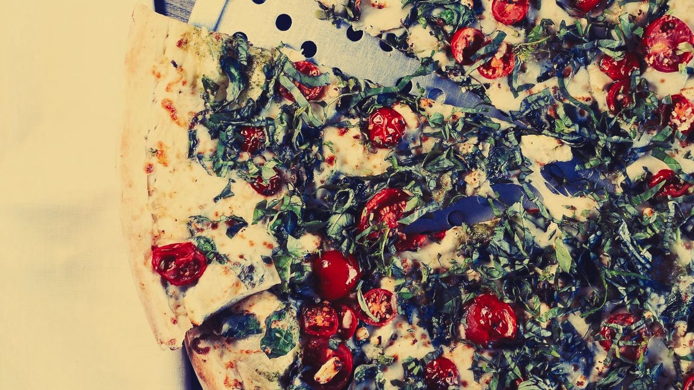 A pizza with spinach , tomatoes and cheese on it