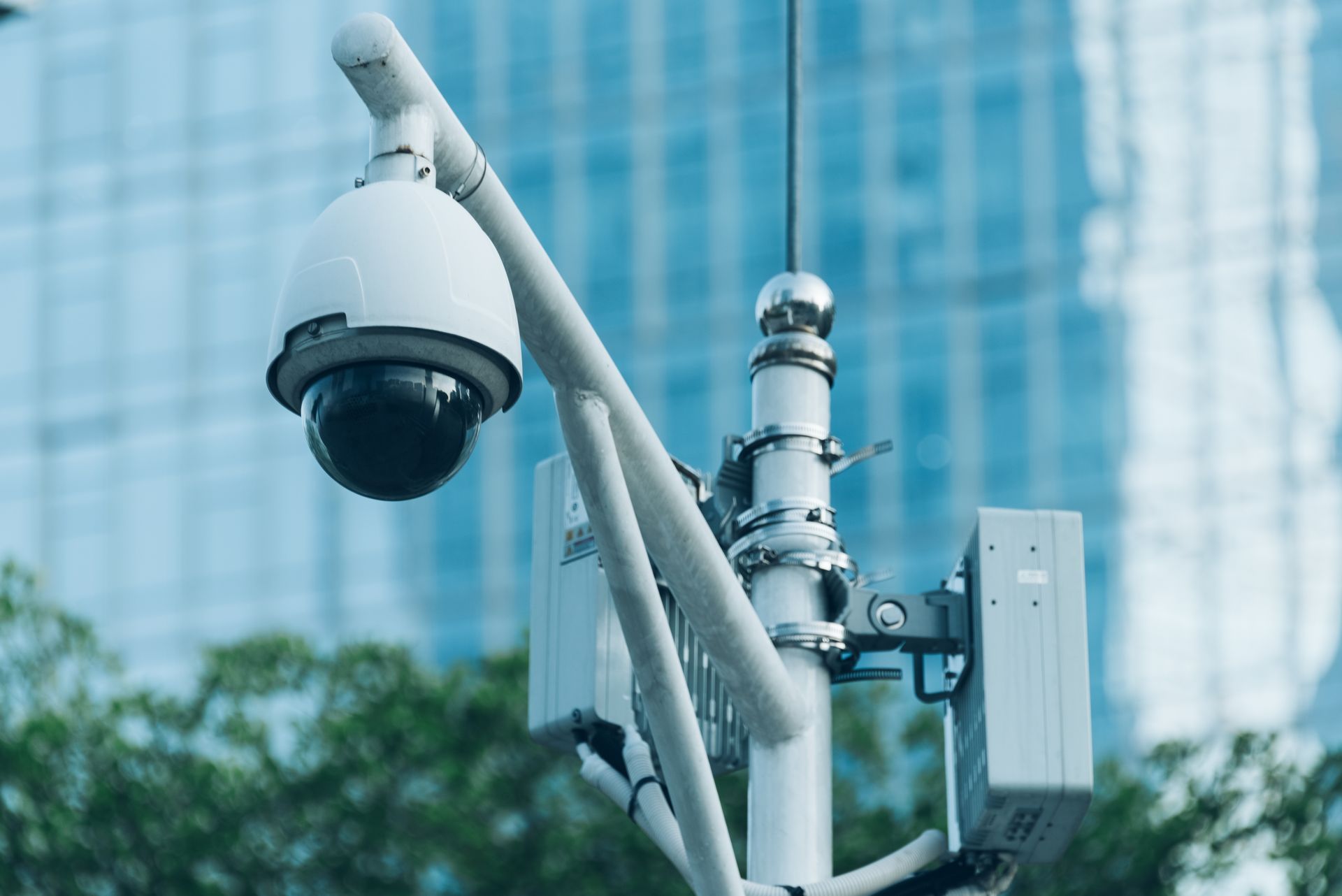 Security camera on a pole, with a blurred skyscraper in the background.