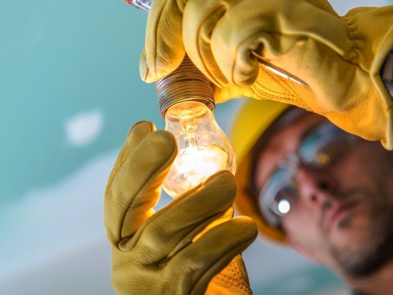 Gloved hands hold a lit light bulb while a blurred technician inspects it in the background