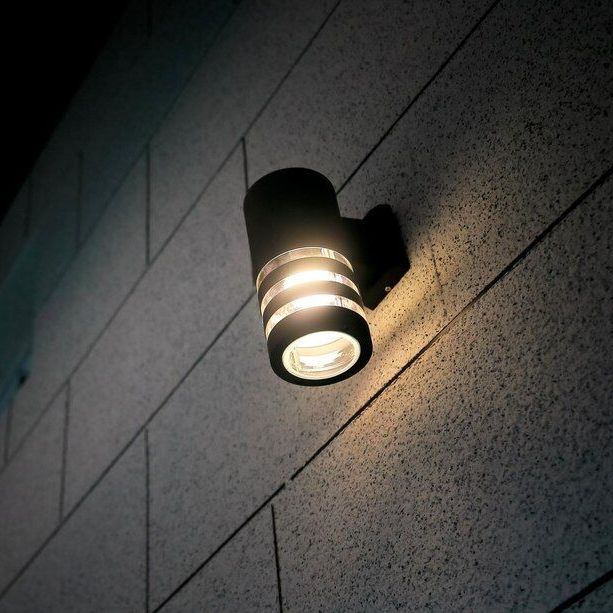 Wall-mounted outdoor light casting a warm glow on a gray tiled wall.