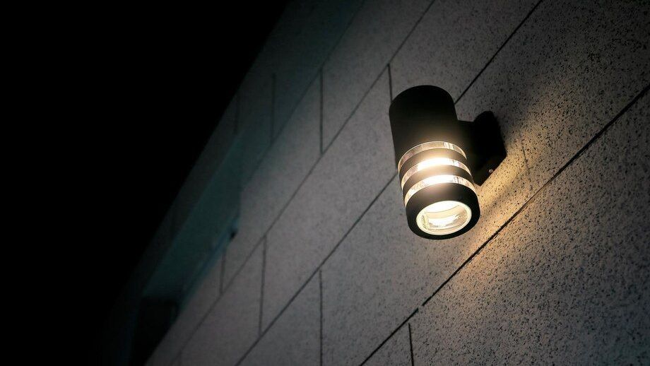 Lit wall-mounted outdoor light on a tiled building at night