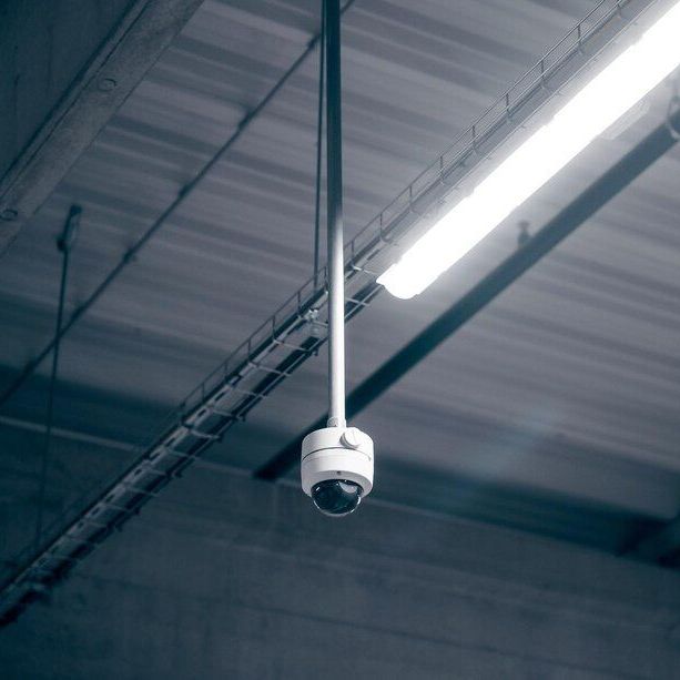 Ceiling-mounted security camera in an industrial warehouse, with bright fluorescent lights overhead