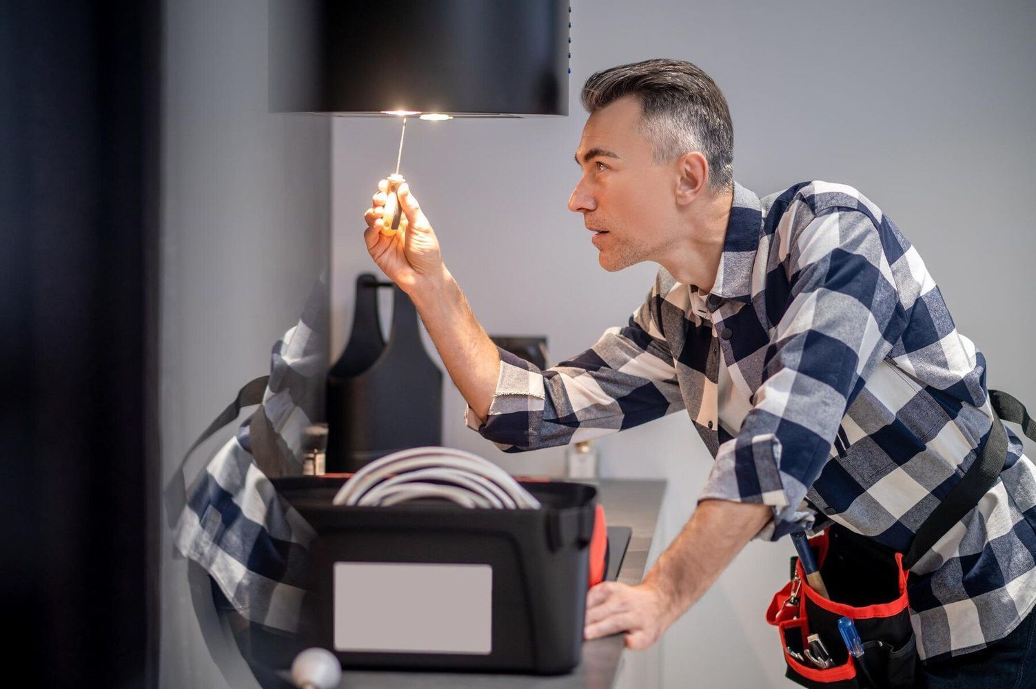 Man holding a lit lighter near a gray wall, inspecting it while working beside a black device.