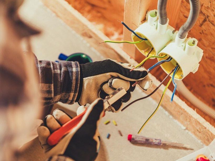 Person wiring an electrical outlet in a wall during home renovation, with exposed colored wires and tools.