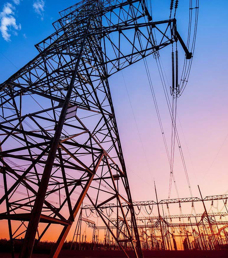 High-voltage power lines and transmission towers at sunset, silhouetted against a pink-orange sky