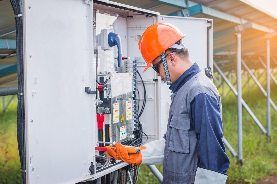 Technician in orange hard hat inspecting an electrical panel outdoors