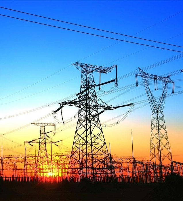 High-voltage transmission towers silhouetted at sunset under a blue-orange sky.