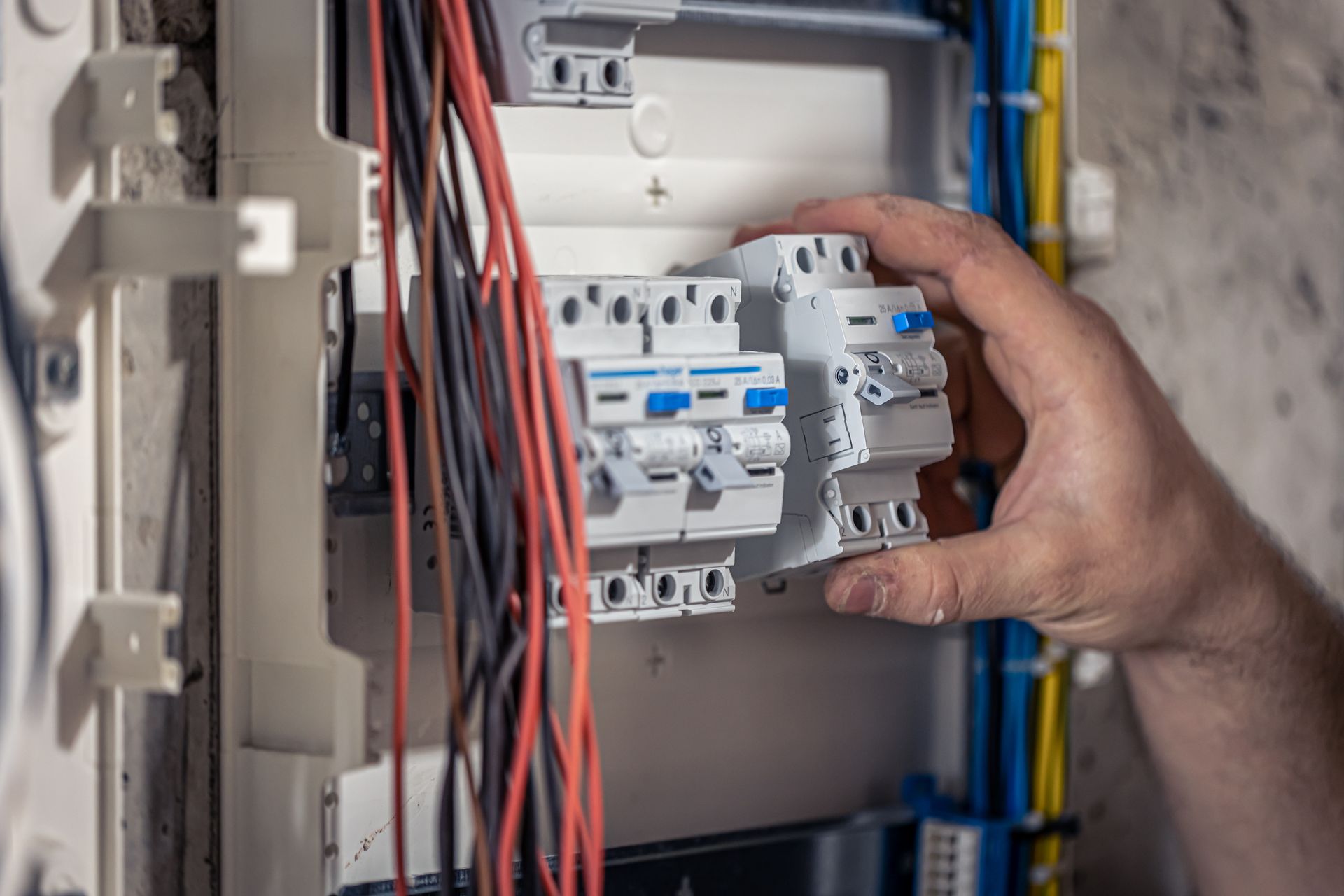 Hand installing electrical circuit breakers in a panel with colored wires.