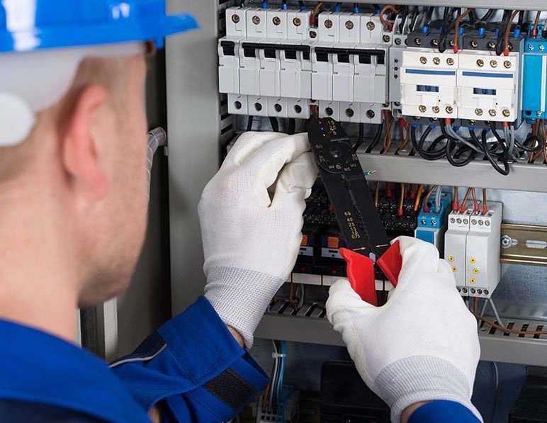 Electrician in hard hat and gloves using pliers to work on a breaker panel
