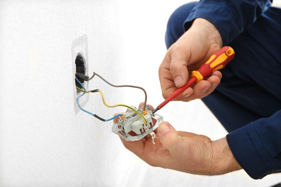 Electrician wiring an outlet with a screwdriver in a wall junction box