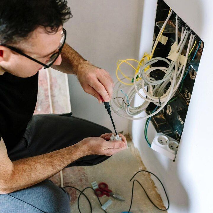 Technician testing cables in an open wall electrical panel with tangled wires