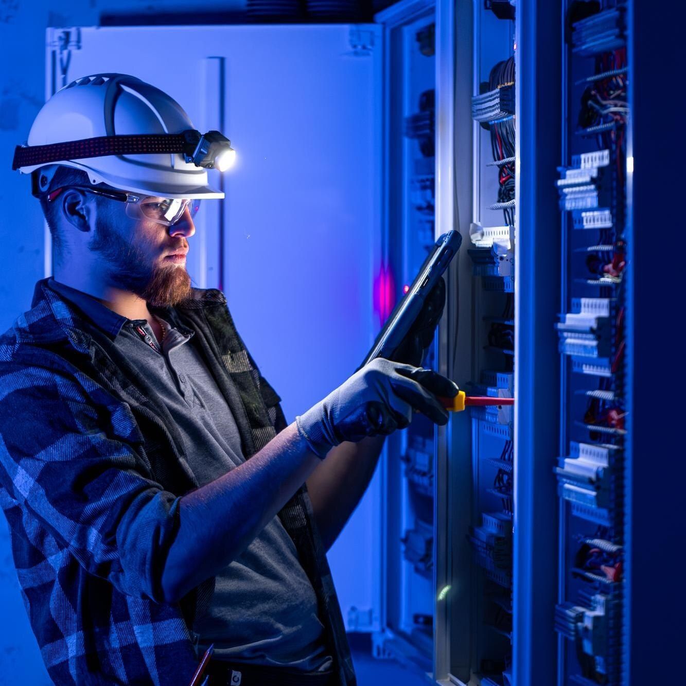Technician in a hard hat using a tablet beside glowing server racks in a blue-lit data center