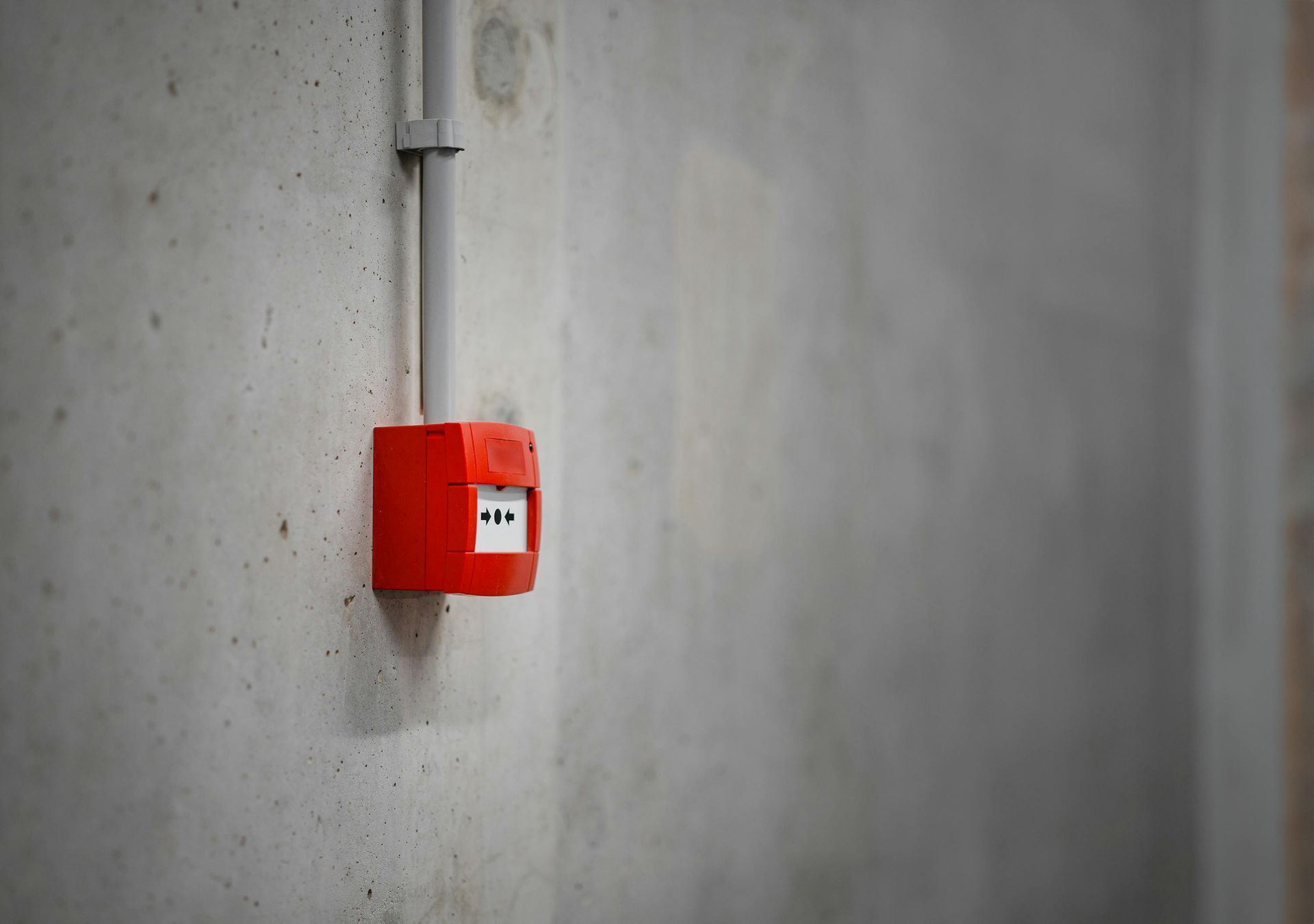 Red fire alarm on a gray concrete wall, electrical conduit above.