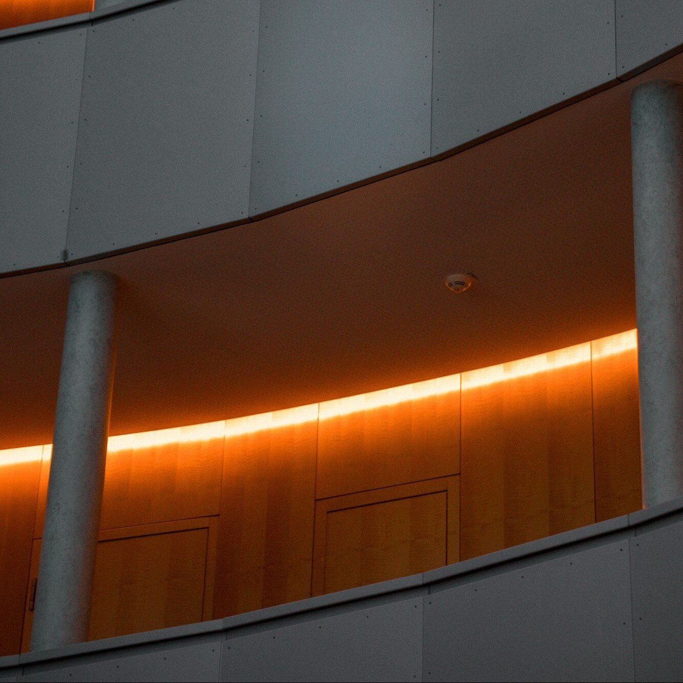 Curved building interior with orange-lit balcony and gray columns