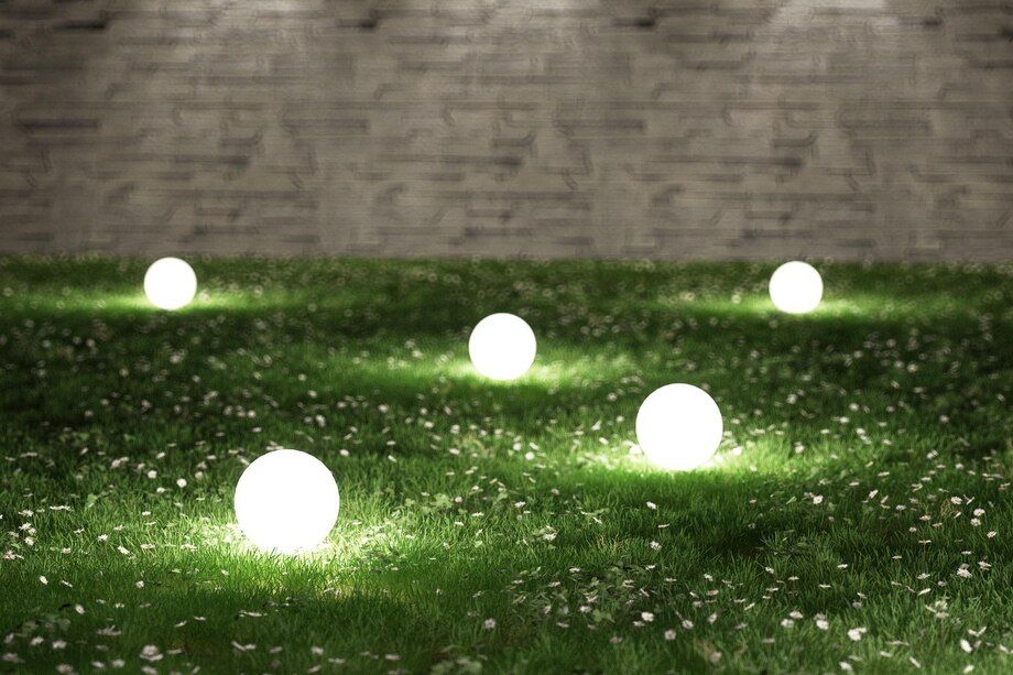 Glowing white orbs scattered on a grassy lawn at night, with a stone wall in the background