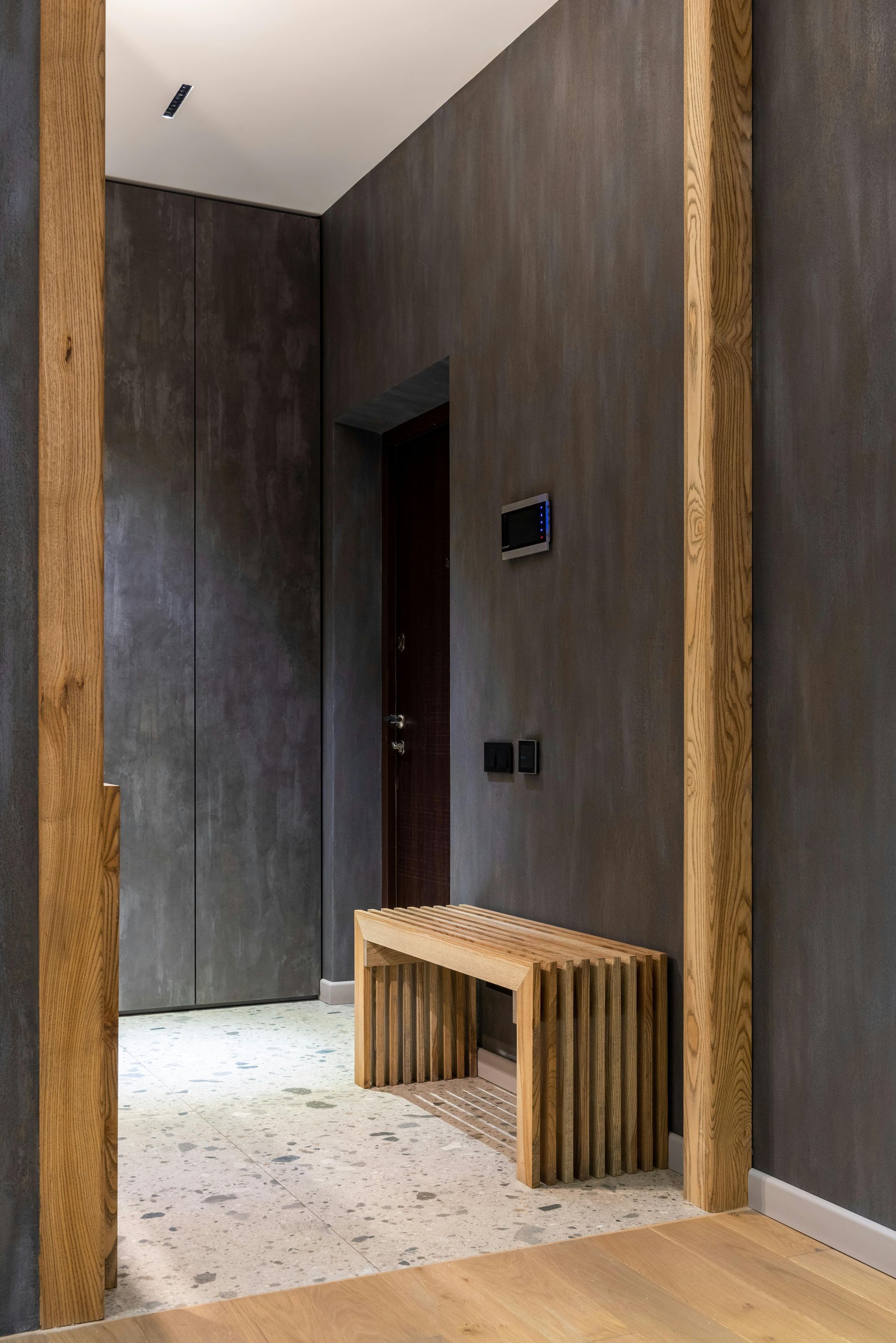 Modern entryway with a dark grey wall, wooden bench, and light-colored floor.