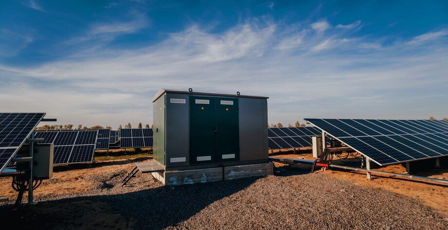 Solar farm with rows of panels and a central battery storage unit under a blue sky