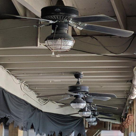 Row of ceiling fans with light fixtures hanging under a covered outdoor walkway