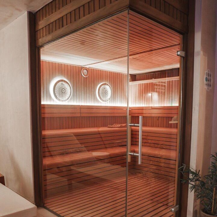 Wood-paneled infrared sauna with glass door and two round wall clocks