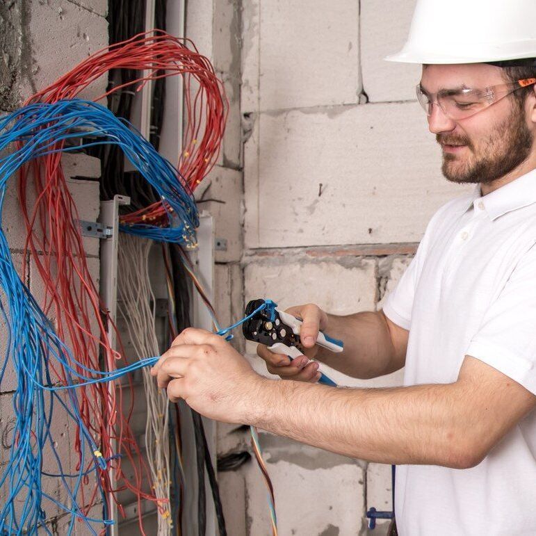 Electrician cutting wires, wearing a hard hat and safety glasses, inside a building.