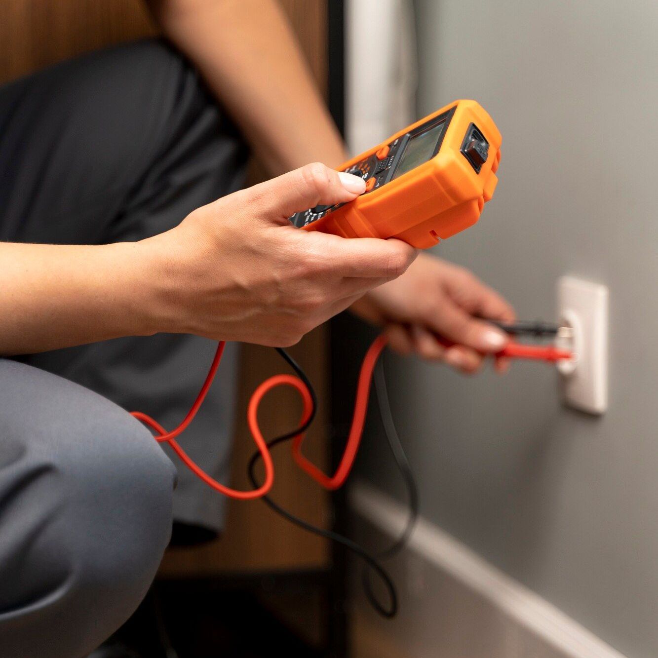 Person using an orange multimeter to test an electrical outlet with red probes