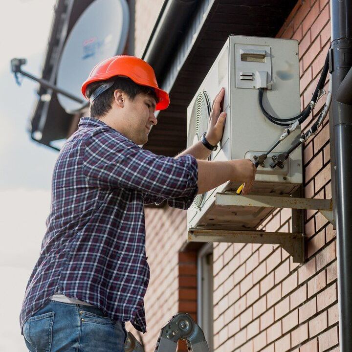 Worker in orange hard hat installing an outdoor electrical unit on a brick wall