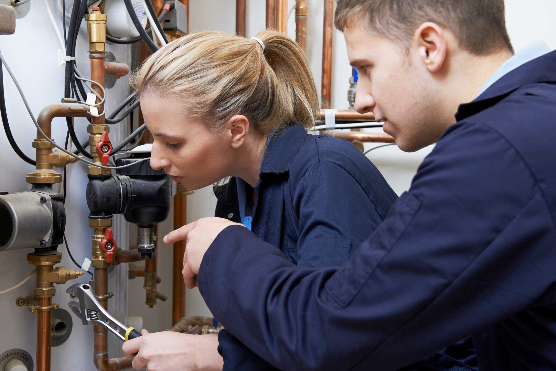 Female trainee plumber working on central heating boiler.