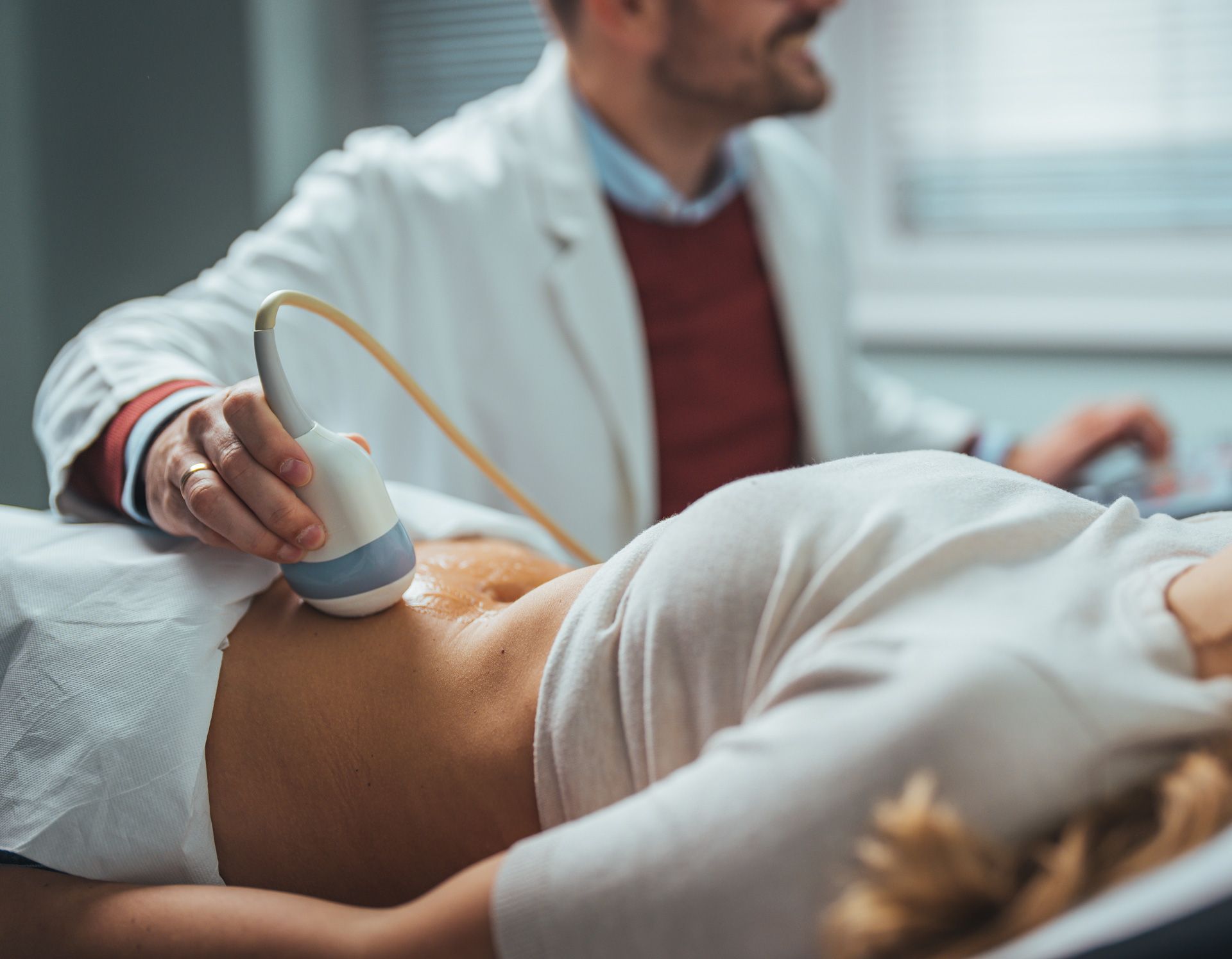 A medical professional performs an abdominal ultrasound on a patient lying on an exam table.