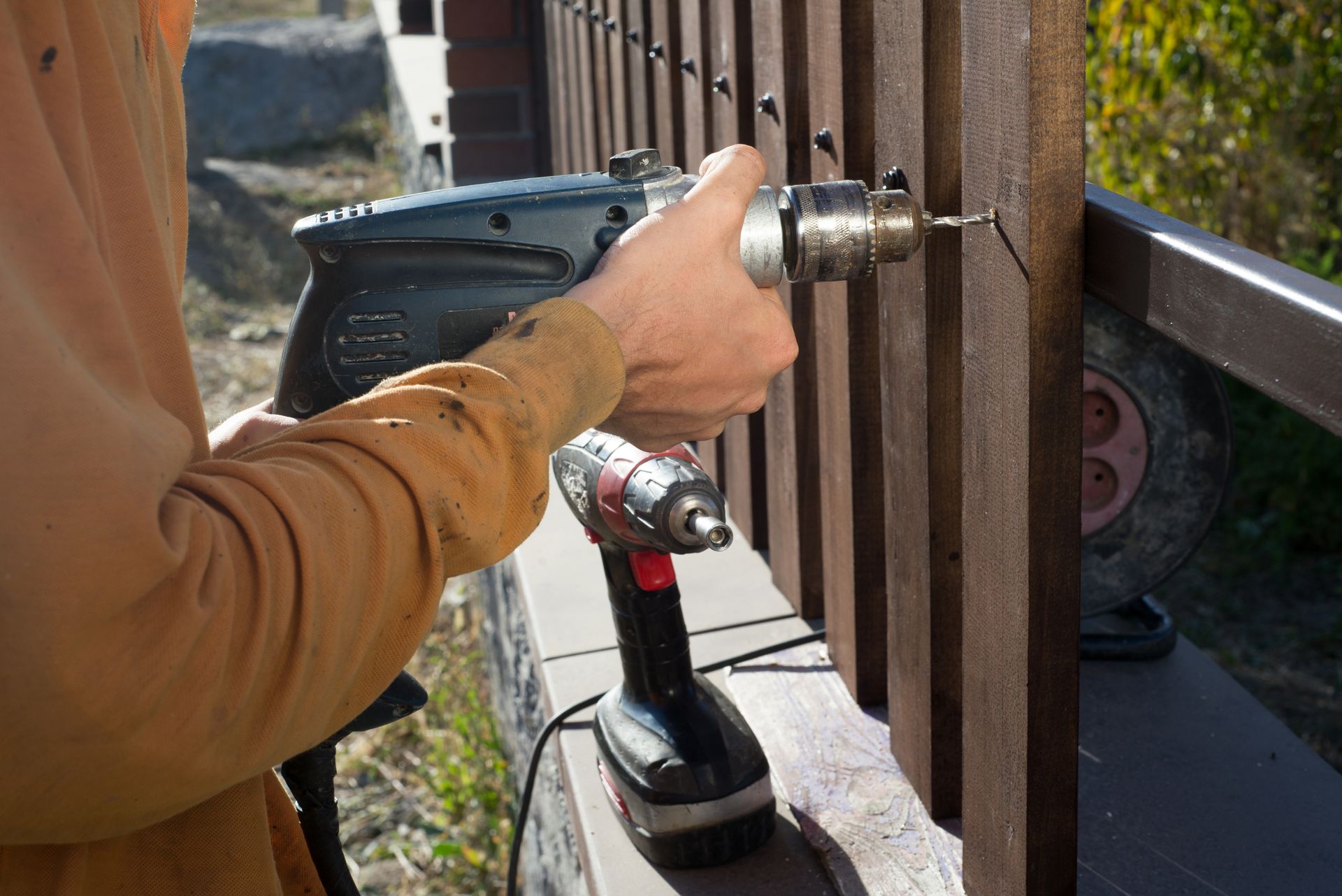 A worker using a power drill to install a vertical wooden fence. A worker using a power drill to install a vertical wooden fence.