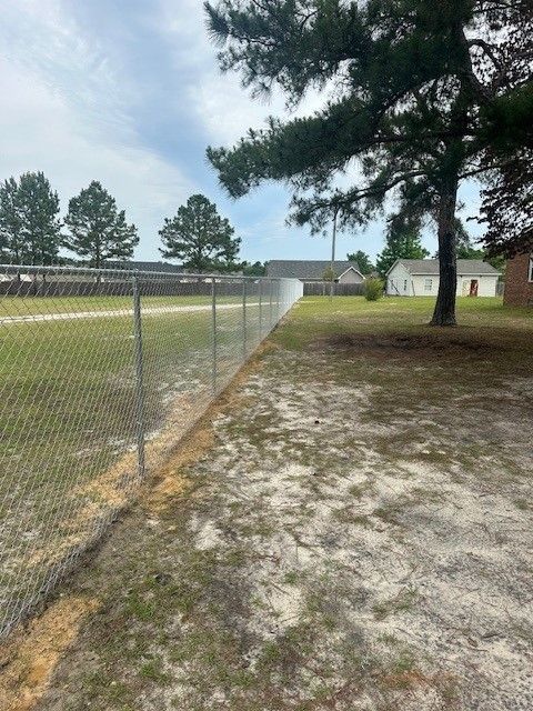 A chain link fence surrounds a dirt field with trees in the background