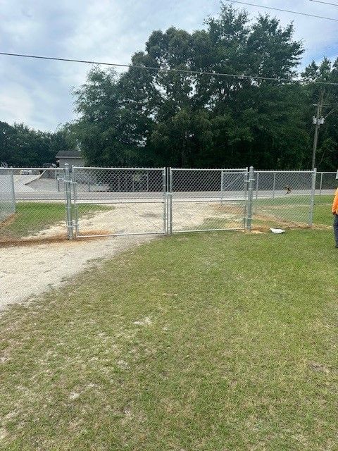 A man in an orange shirt is standing in front of a chain link fence