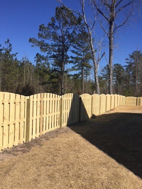 A wooden fence surrounds a yard with trees in the background.