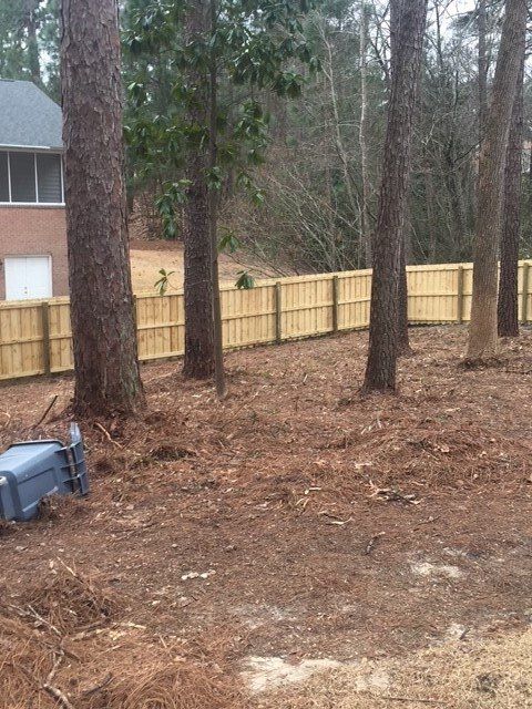 A wooden fence is surrounded by trees in a yard.