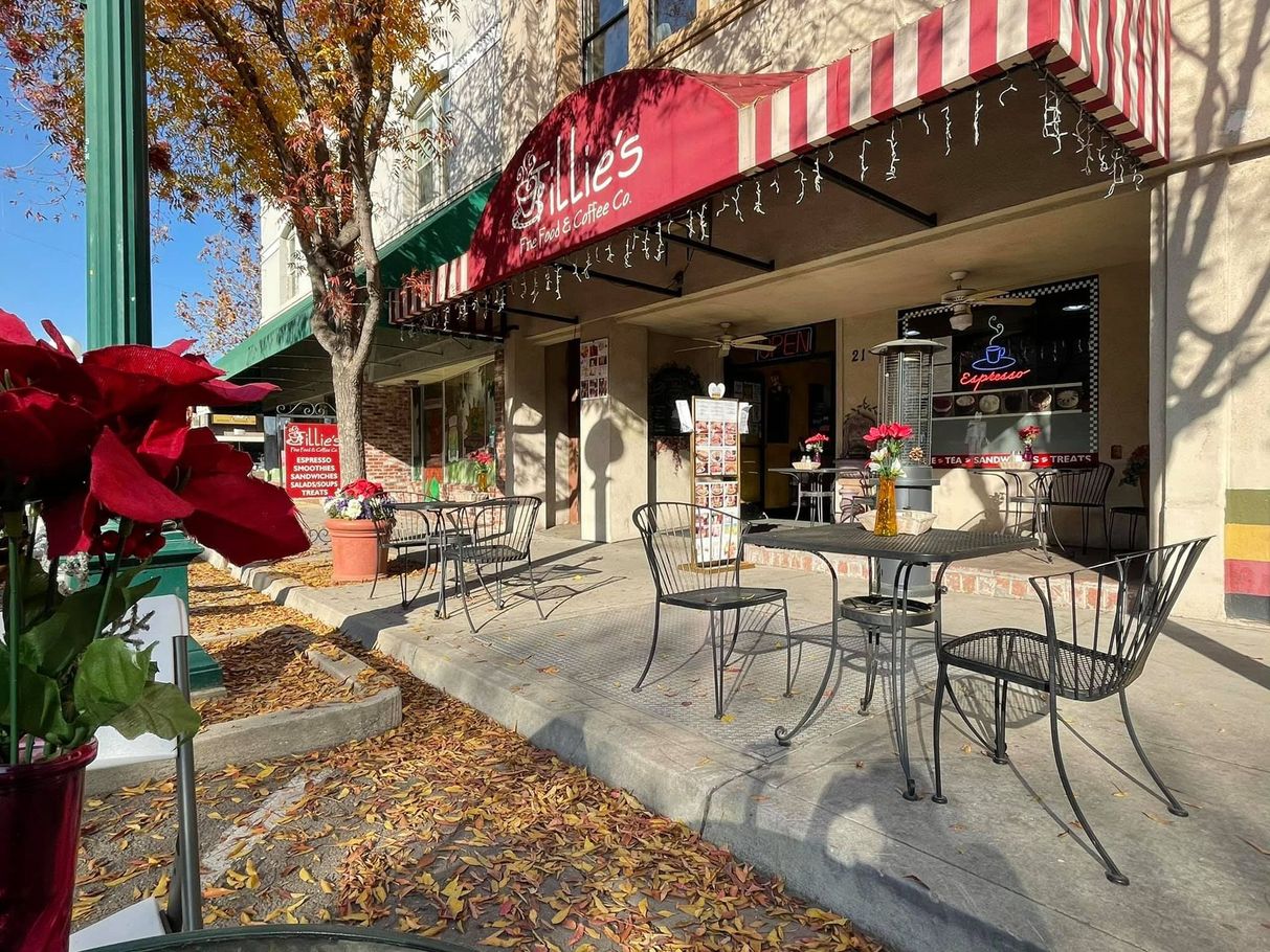 Outdoor café patio with red awning, metal tables and chairs, and fallen autumn leaves on the sidewalk.