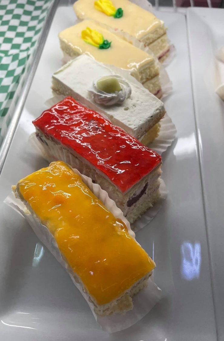Assorted colorful rectangular dessert slices on a white plate, topped with glaze and fruit garnish