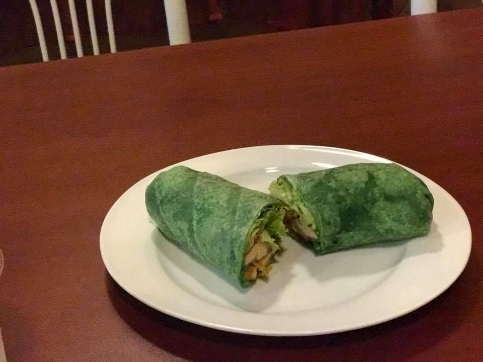 Green wrap cut in half on a white plate on a wooden table.