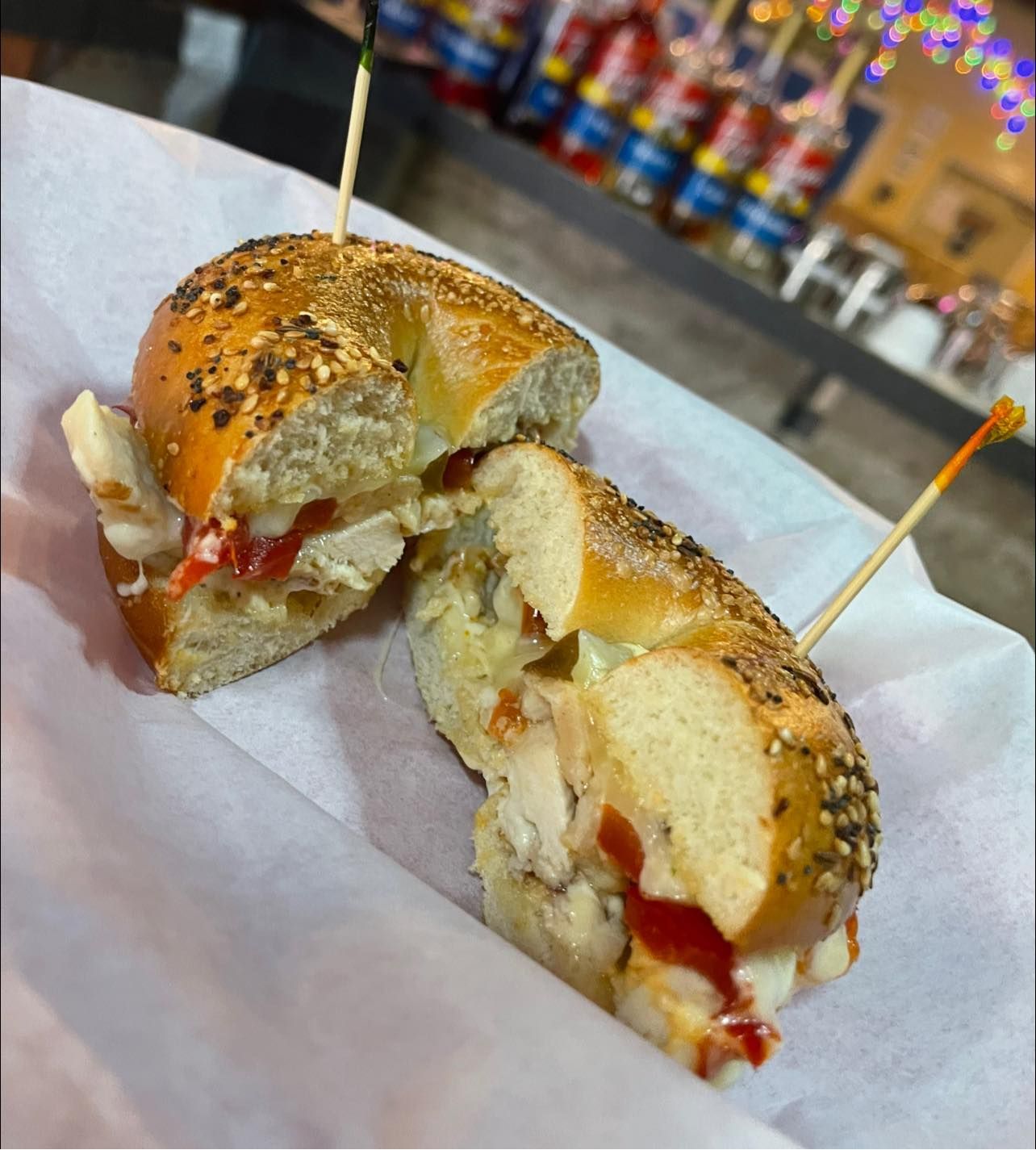 Sliced sesame bagel sandwich with melted cheese and tomato on parchment paper, toothpicks in each half.