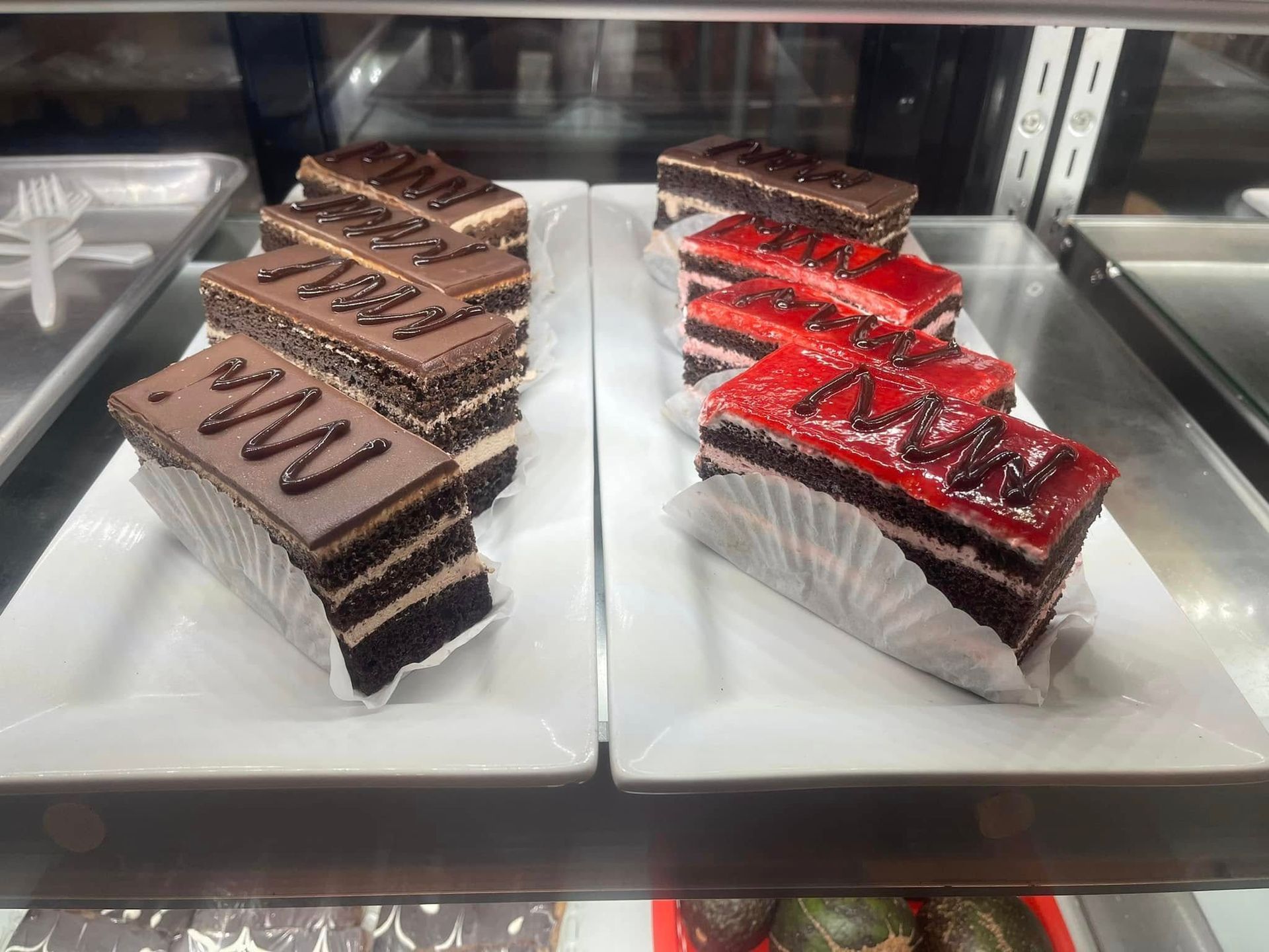 Slices of chocolate and strawberry cake displayed in a glass bakery case