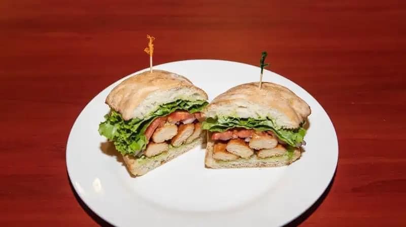 Sandwich halves with shrimp and lettuce on a white plate against a red table