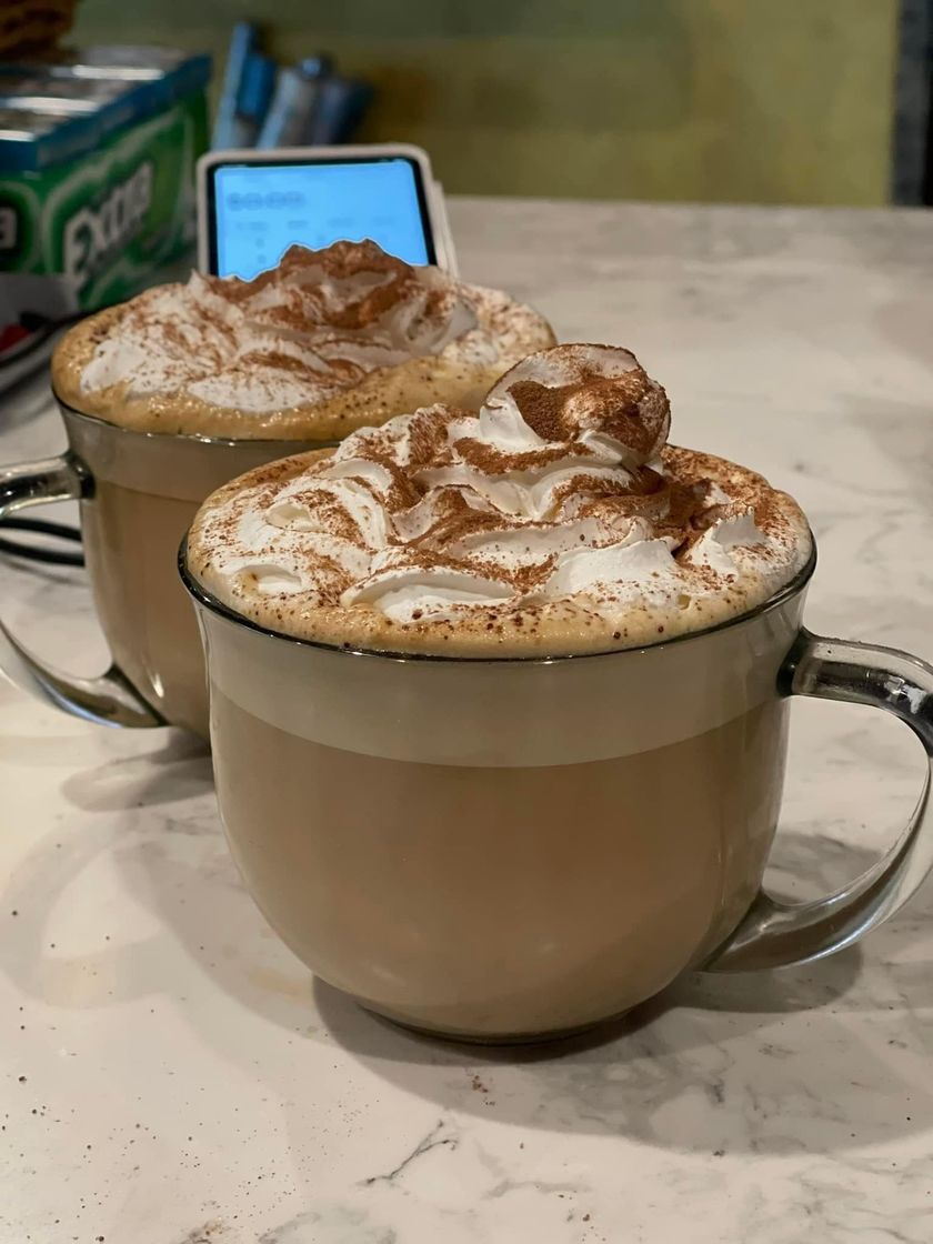 Two mugs of coffee topped with whipped cream and cinnamon on a table