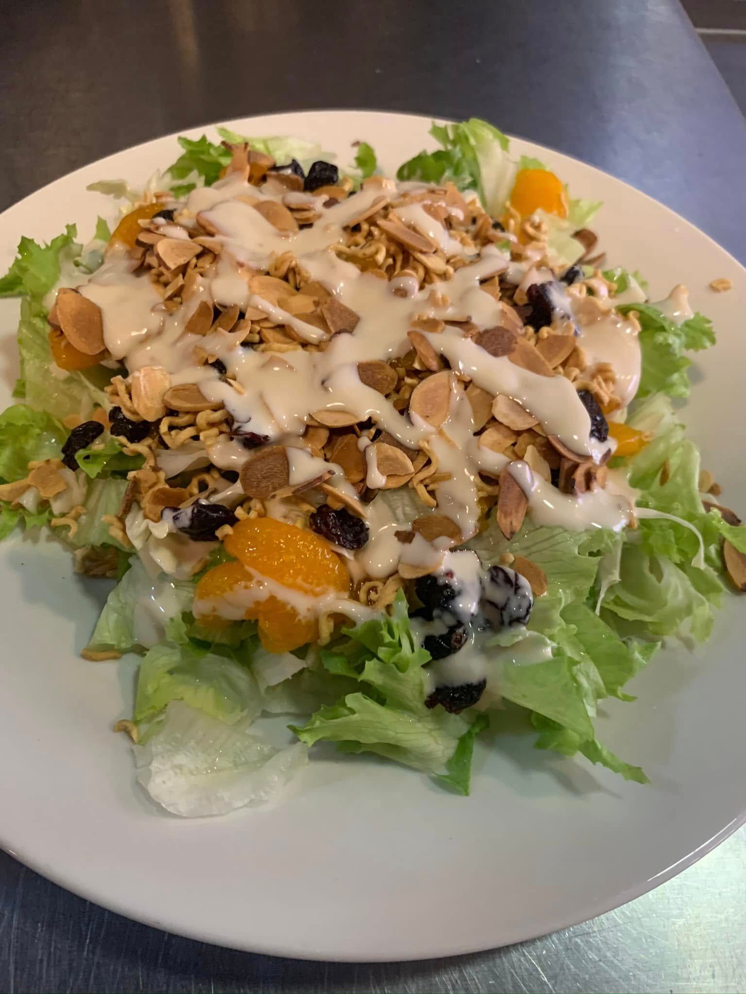 Salad with lettuce, oranges, olives, nuts, grilled chicken, and creamy dressing on a white plate.