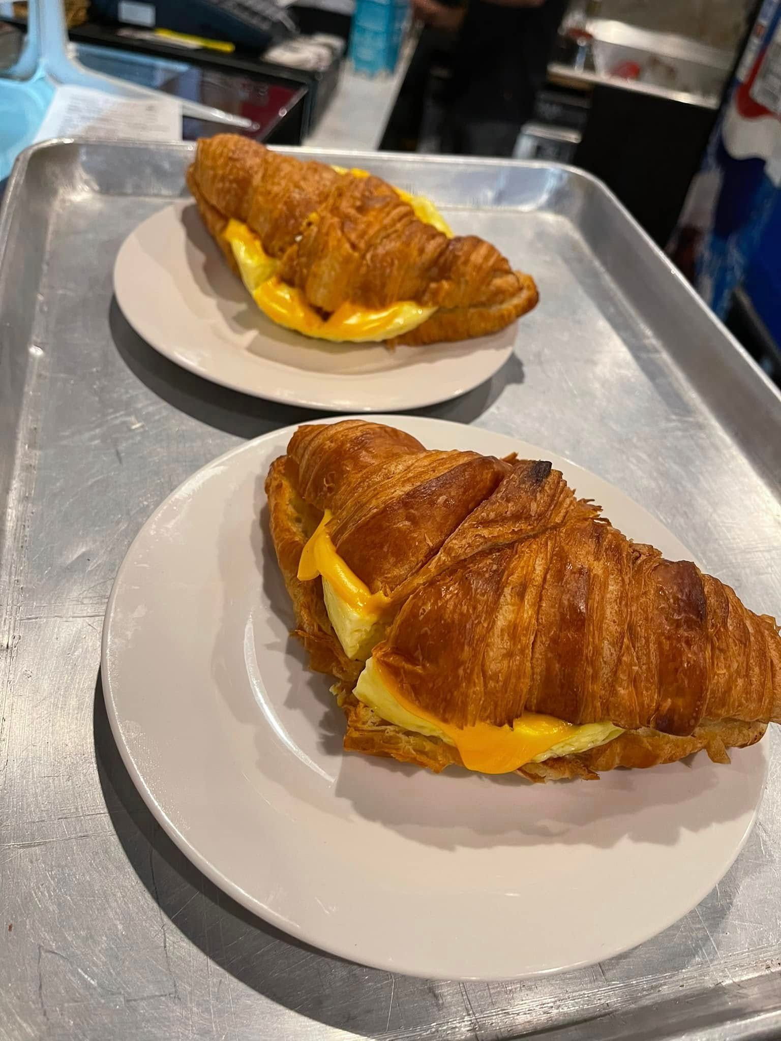 Two croissants filled with melted cheese on white plates atop a metal tray