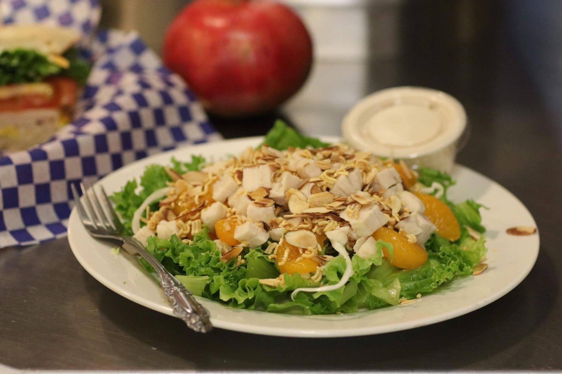 Salad with greens, almonds, and orange slices on a white plate beside a fork and dressing cup