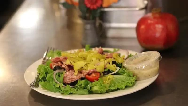 Salad on a white plate with greens, tomatoes, and dressing on a kitchen counter