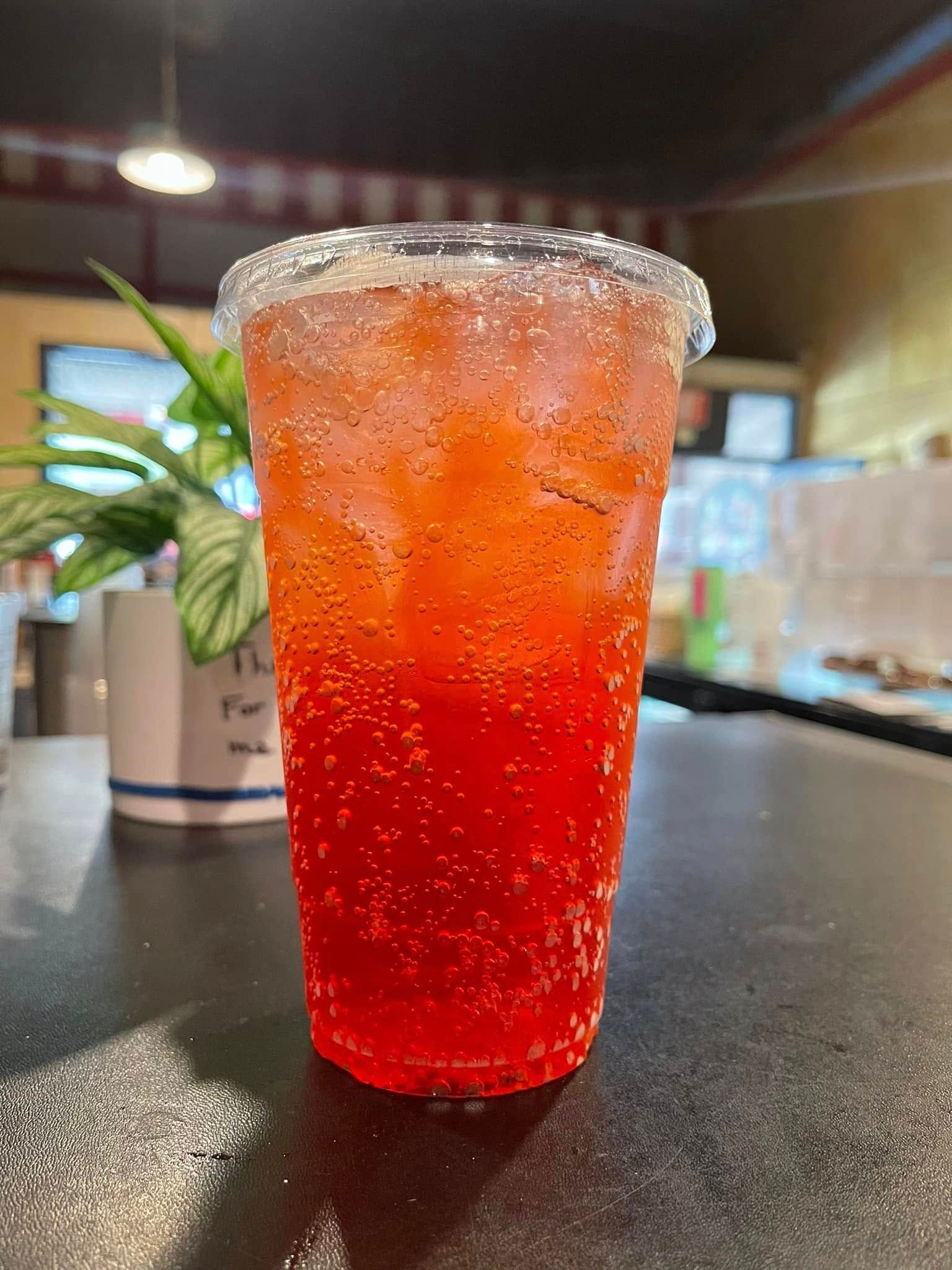 Red iced drink in a clear plastic cup with a salted rim on a dark counter, with a potted plant blurred behind it