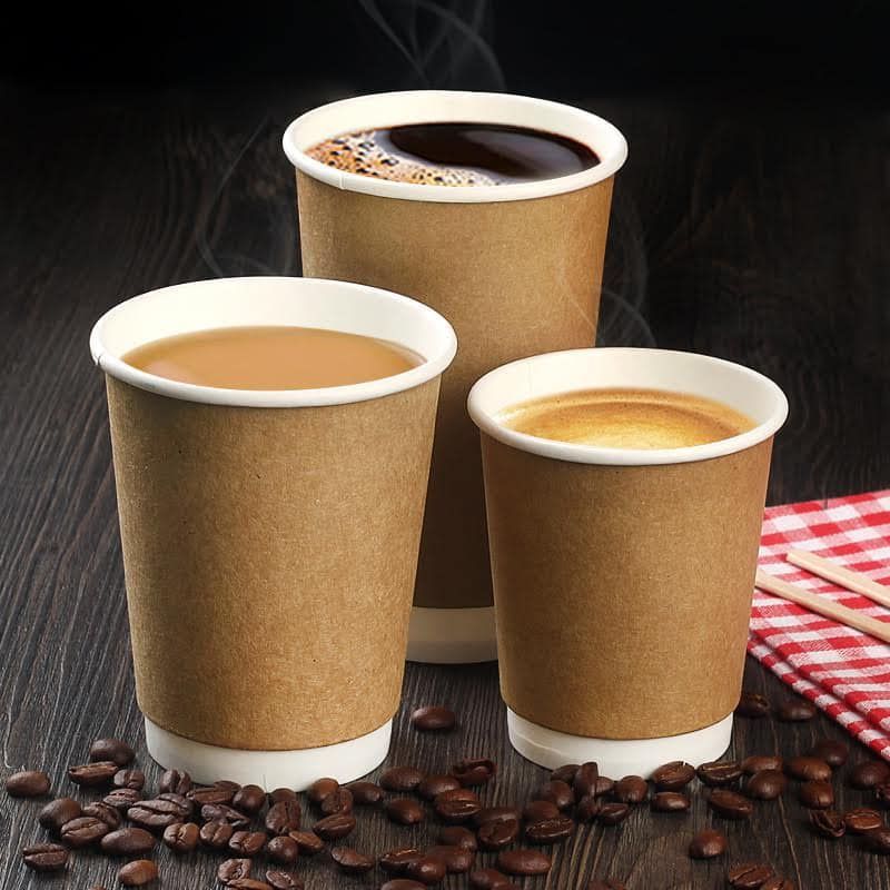 Three takeaway coffee cups on a dark table with coffee beans and a red checkered napkin