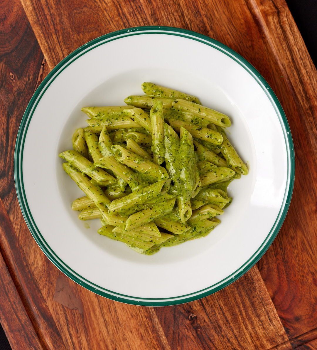 a bowl of pasta with green sauce on a wooden table