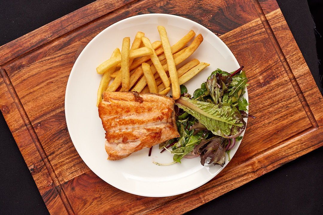 Salmon with french fries and a salad on a wooden cutting board