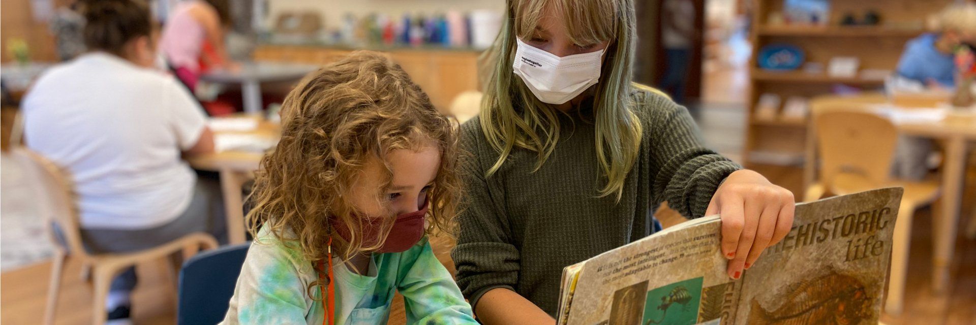 Older child sitting with younger child and Prehistoric Life book