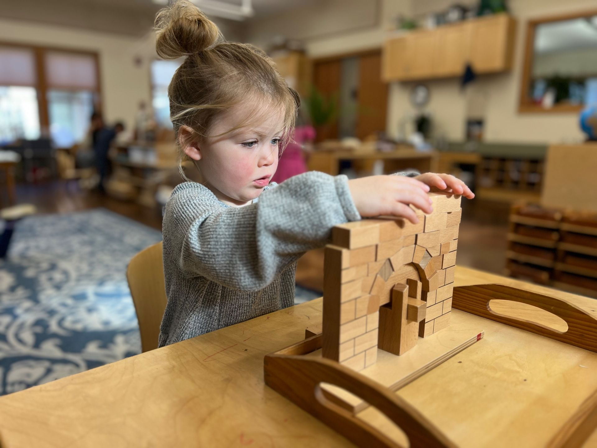 image of a preschool aged child sitting at a table with a tray with blocks built into the Roman Arch